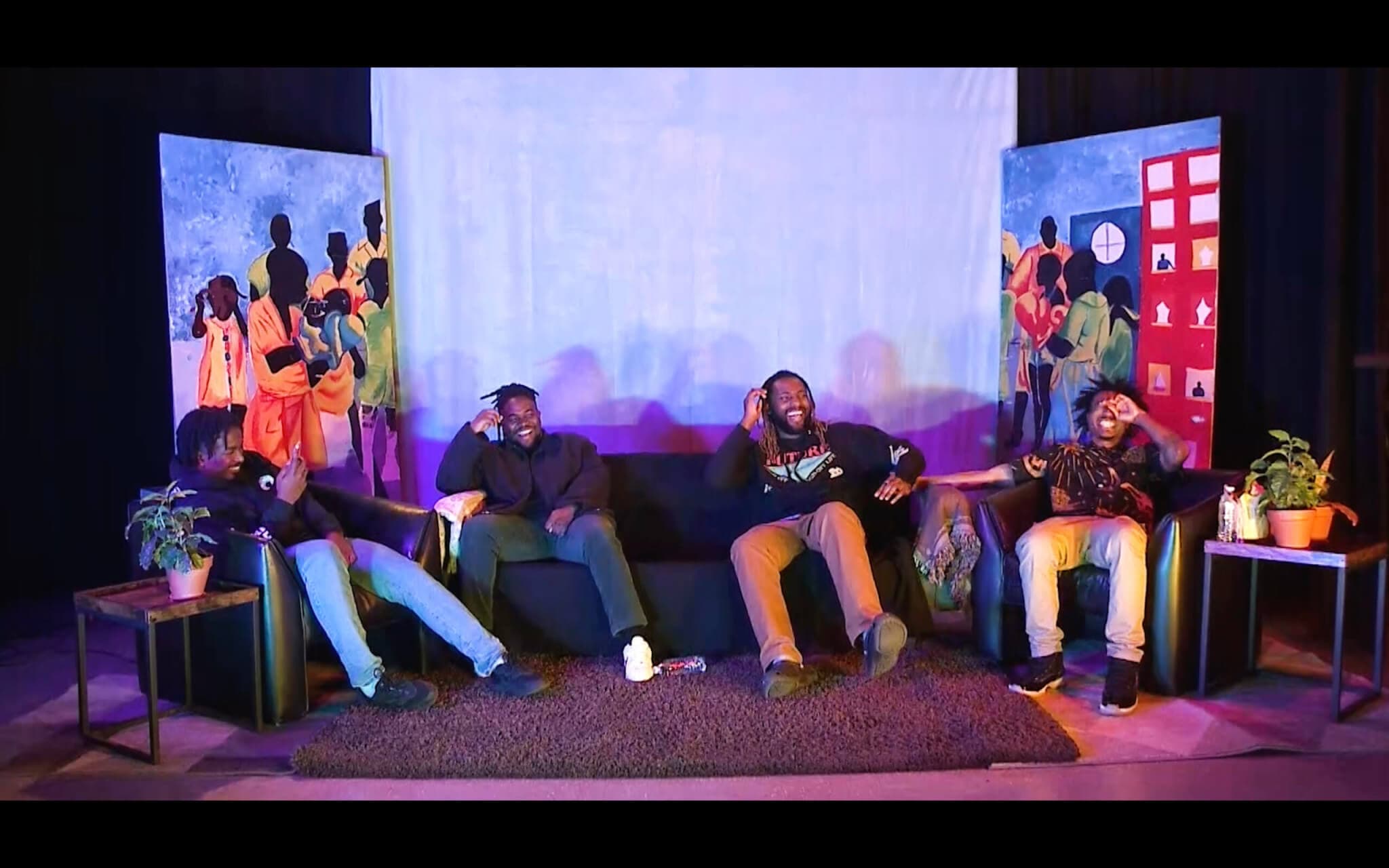 Circle Squared collaborators sit on a couch and chairs in front of a backdrop that features figures.