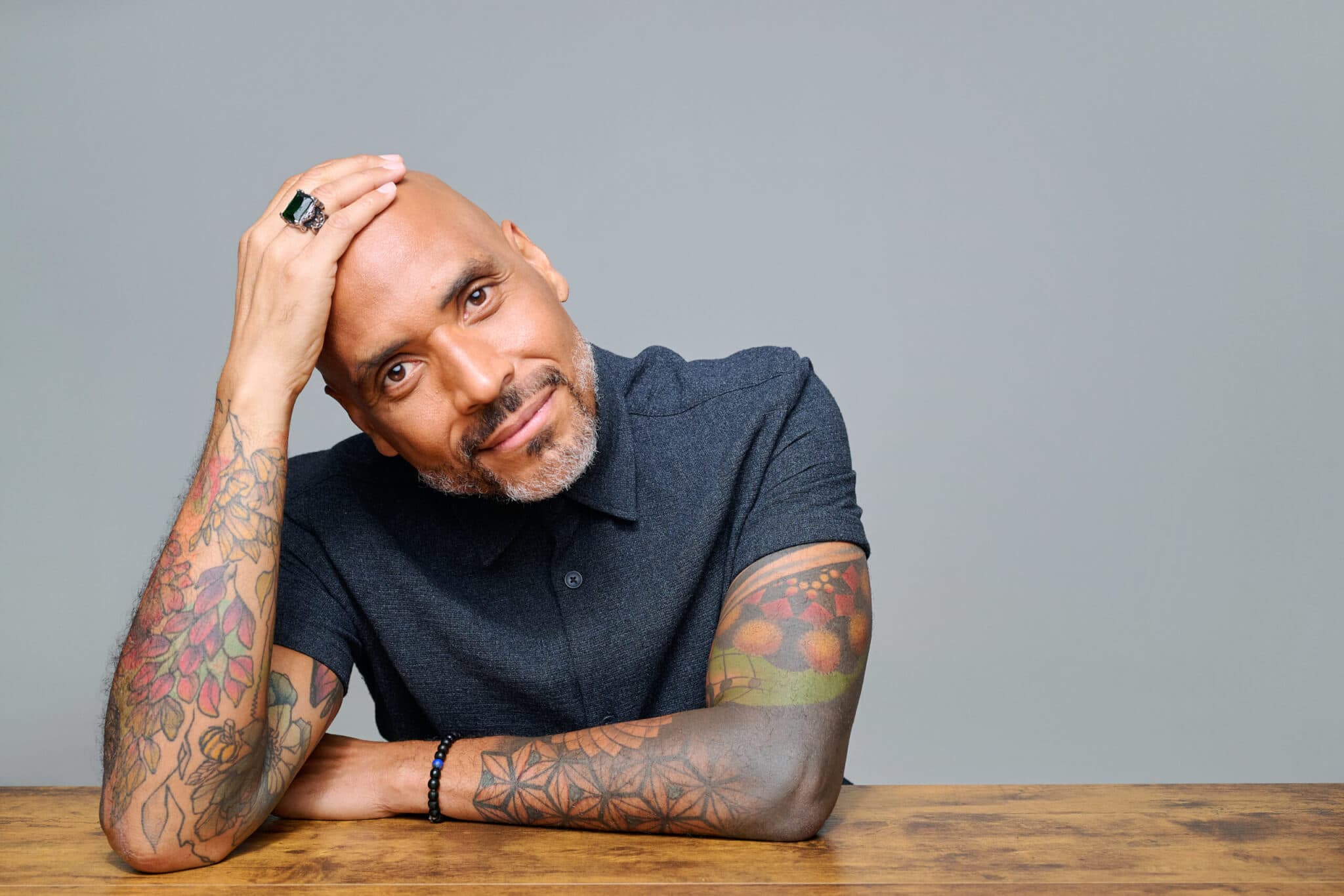 A man seated at a table rests his hand on his head.