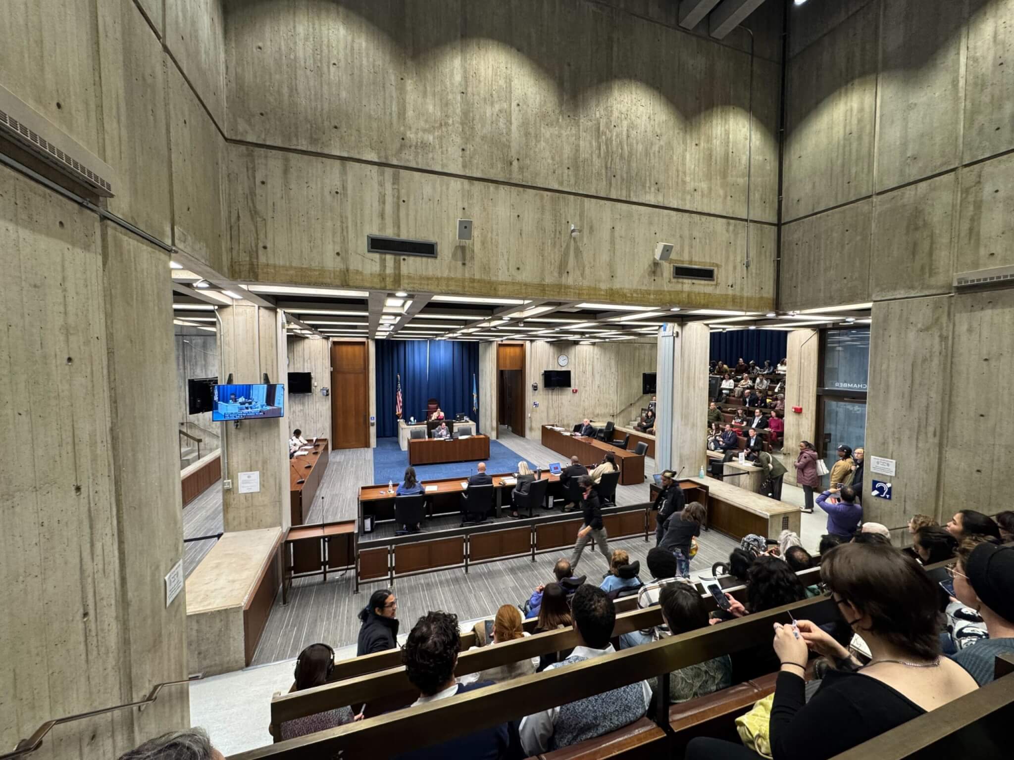 A meeting takes place inside Boston City Council chambers.